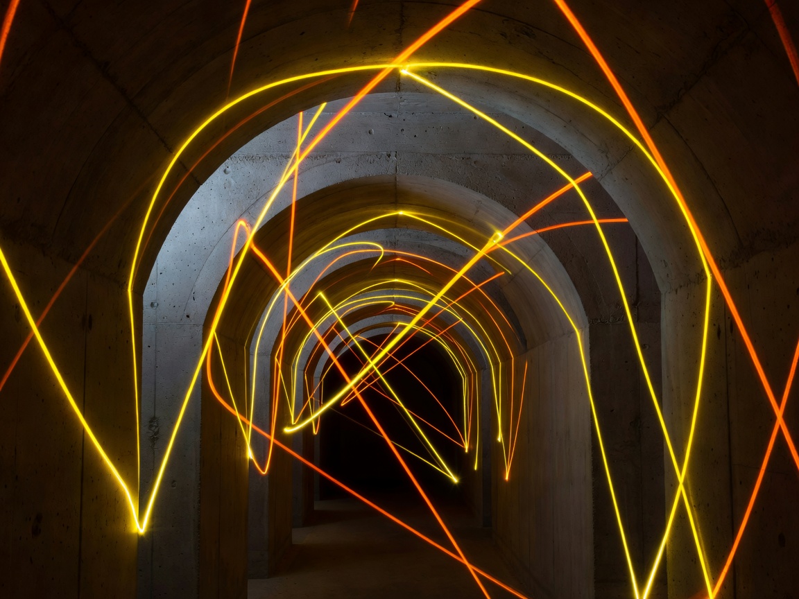 Lumen Corridor showcasing high contrast yellow and orange laser light trails bouncing along raw industrial concrete vaults